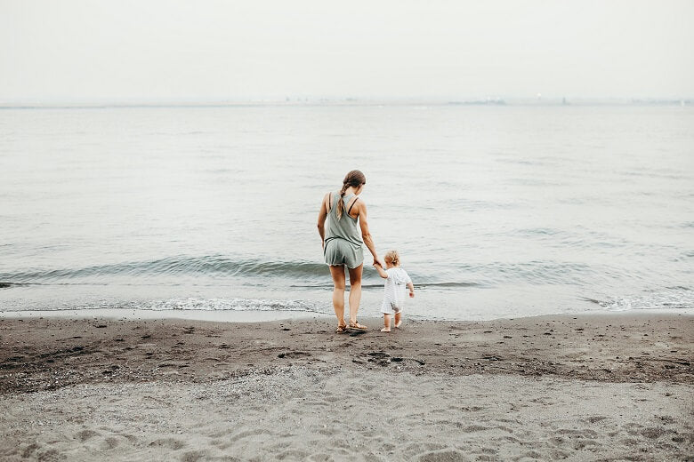 Mother playing with her child at the beach near the ocean, both barefoot